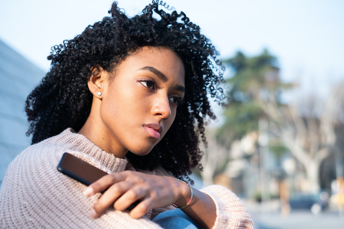 Young BIPOC woman holding phone. Discover how to set boundaries and take back your power.