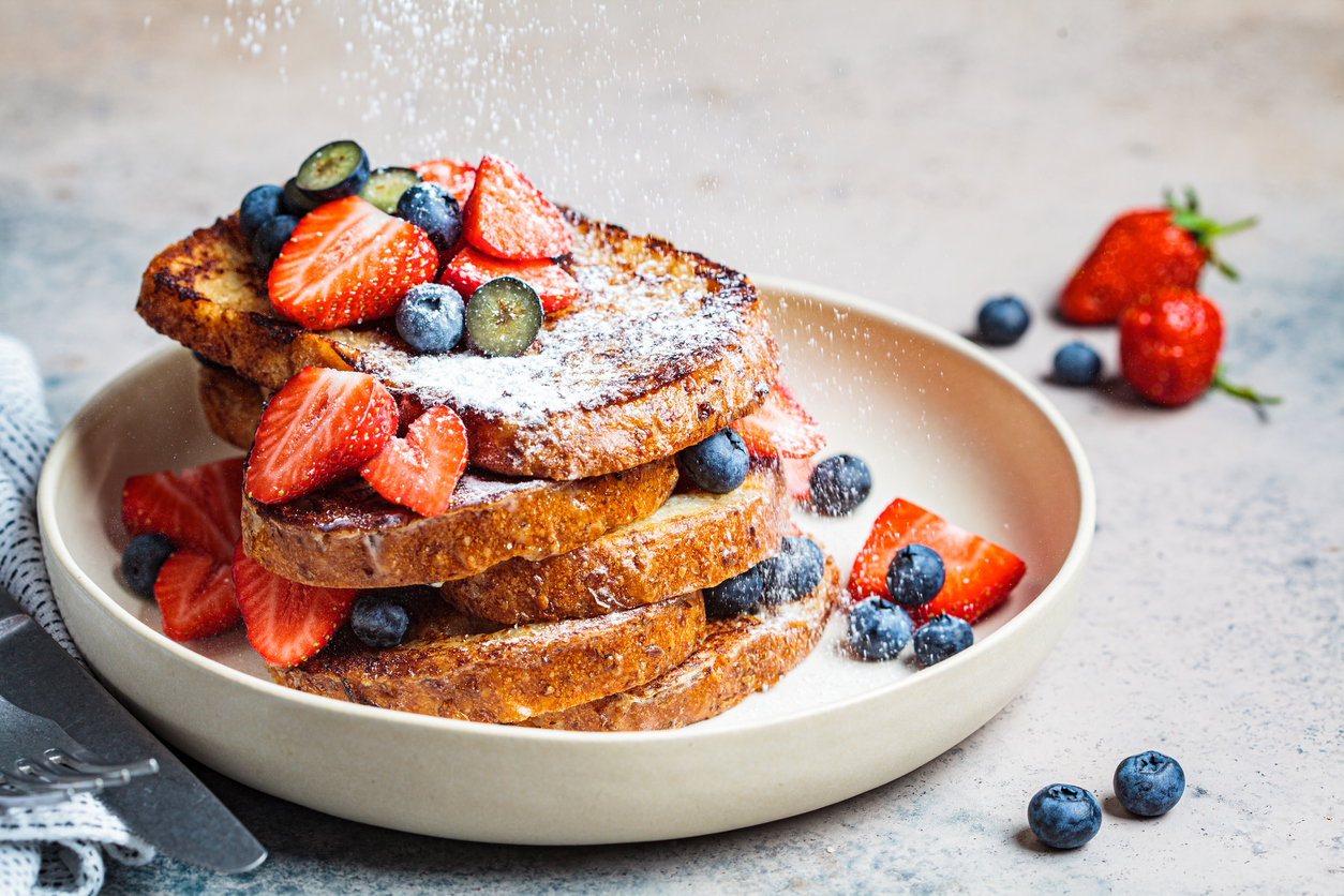 pile of french toast on a white plate with strawberries, blueberries, and powdered sugar