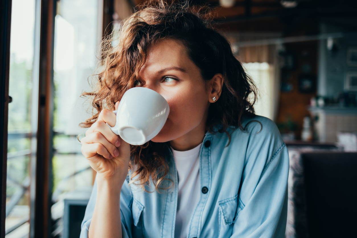 a woman with curly brown hair drinks a beverage out of a coffee cup