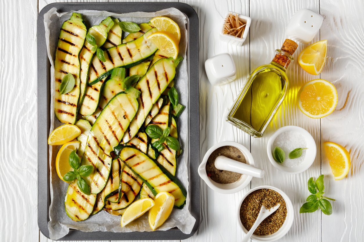 Grilled zucchini and squash slices on a sheet pan with olive oil and lemon slices