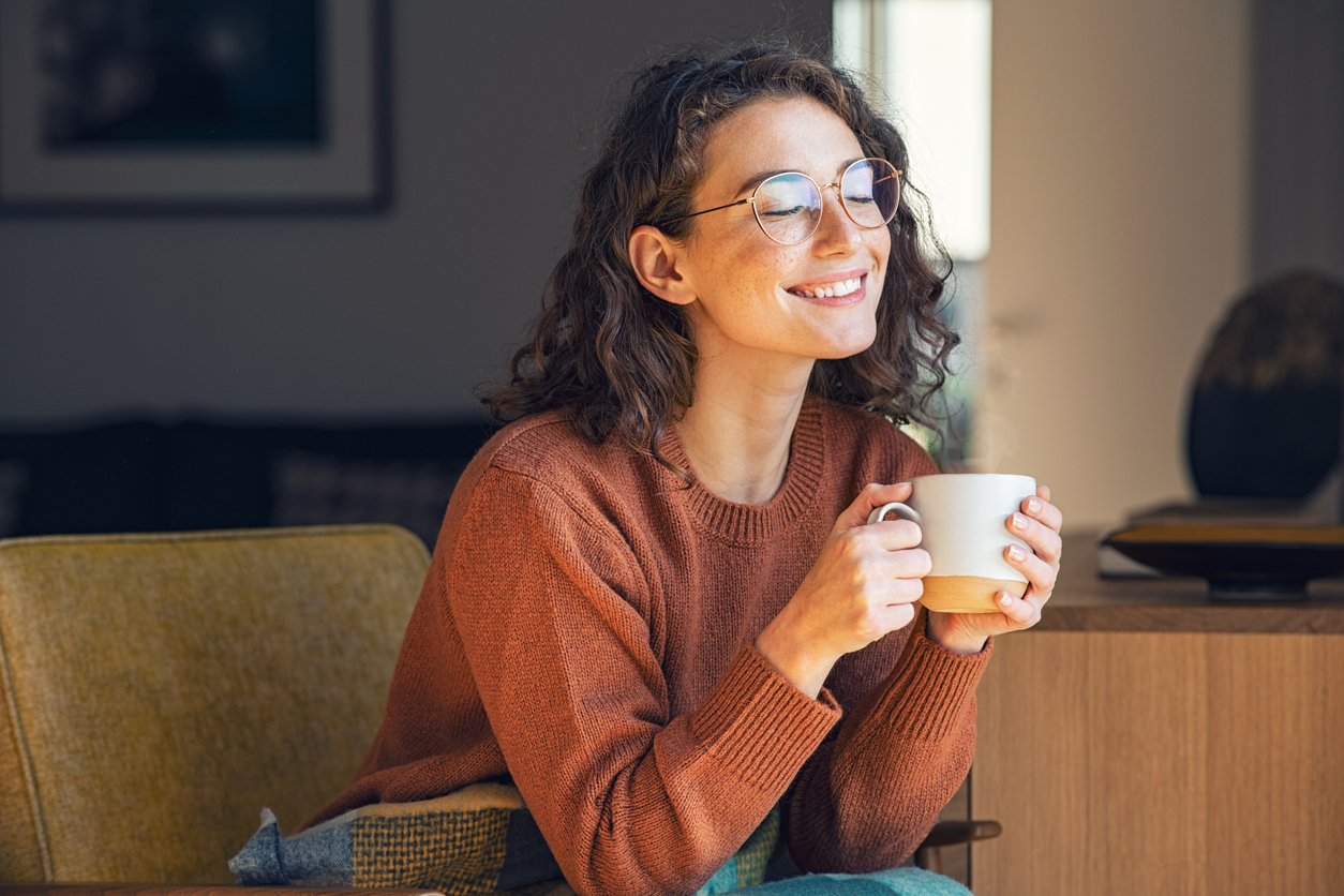 Young woman with curly hair and glasses holding a coffee cup. Find out the best time of day to drink your coffee.