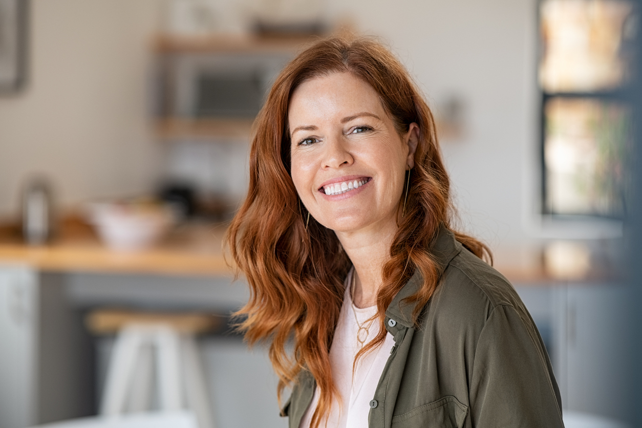 Beautiful woman in her 40s with red hair and a green jacket smiling. Learn when to take progesterone for perimenopause at GloWellmag.com